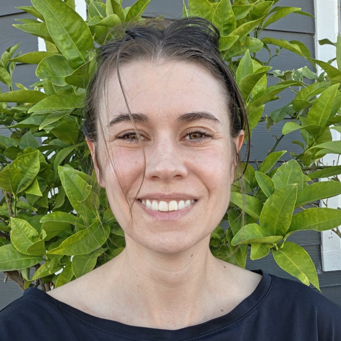 Portrait of Caitria O'Neill outside, in front of citrus leaves, smiling